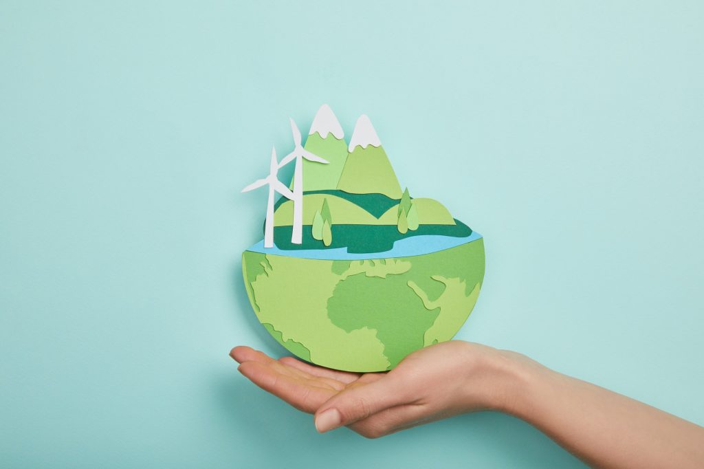 top view of woman holding paper cut planet with renewable energy sources on turquoise background,